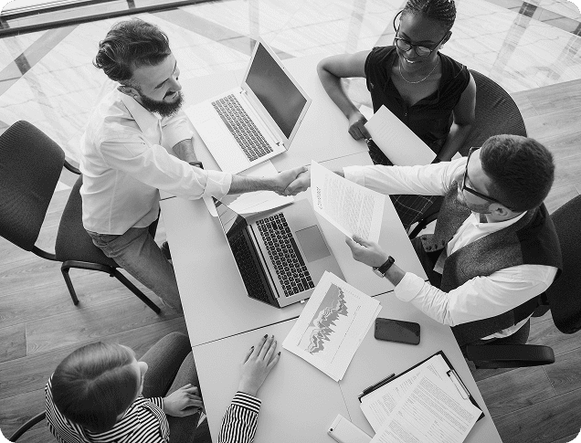 Business professionals engaged in a collaborative financial discussion, shaking hands, with laptops and documents on the table, emphasizing personalized financial strategies and tax planning services.